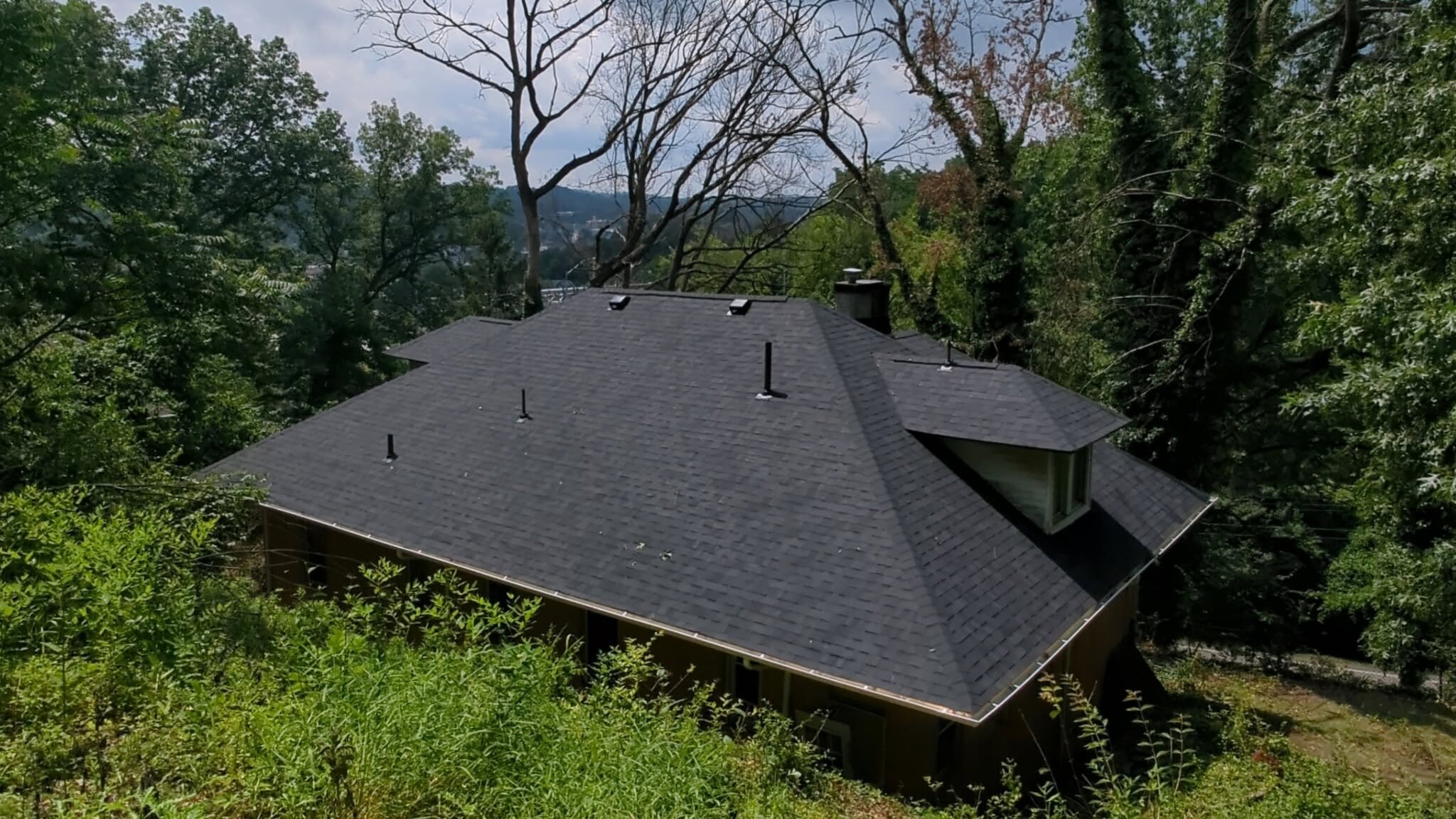 Completed dark shingle roof surrounded by mature trees